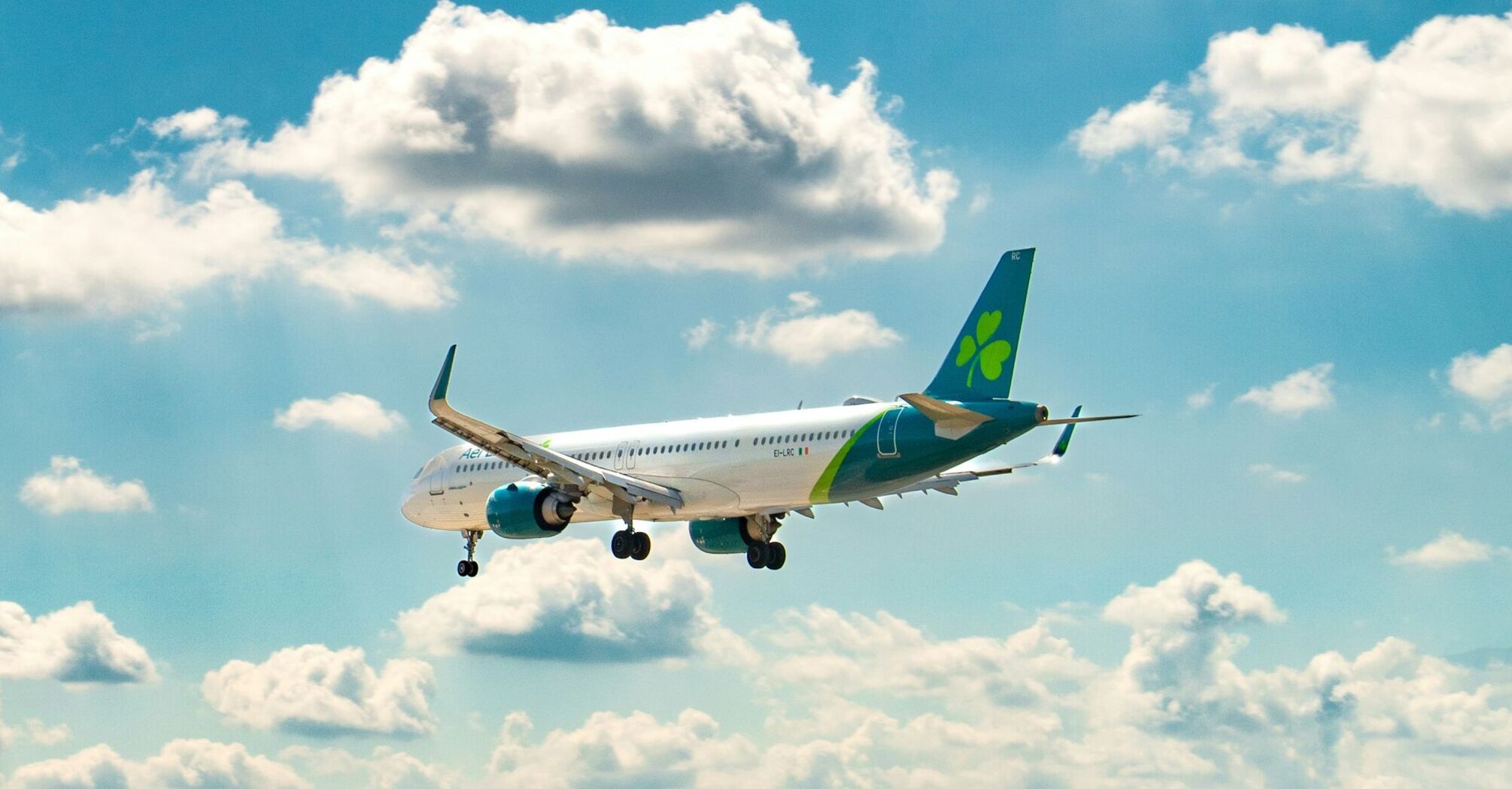 Aer Lingus plane in flight against a bright blue sky with clouds