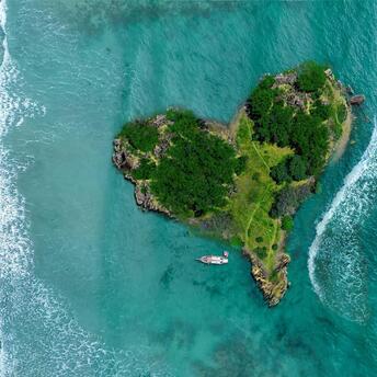 Aerial view of a lush, private island with a boat near a sandy beach