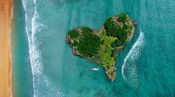 Aerial view of a lush, private island with a boat near a sandy beach