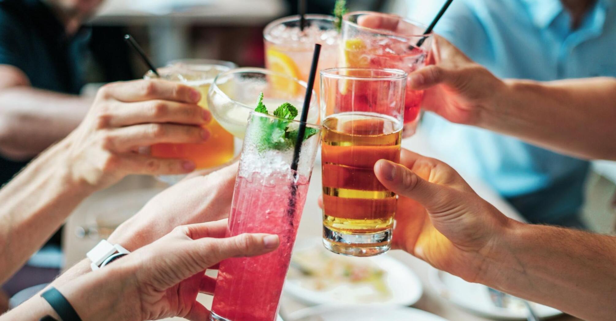 A group of people raising glasses with colorful non-alcoholic beverages in a celebratory toast