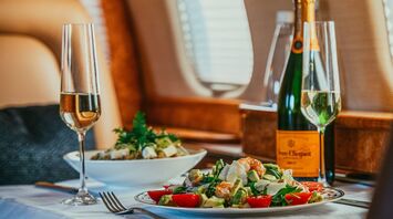 A luxurious in-flight meal served on a private jet, featuring a gourmet salad and champagne