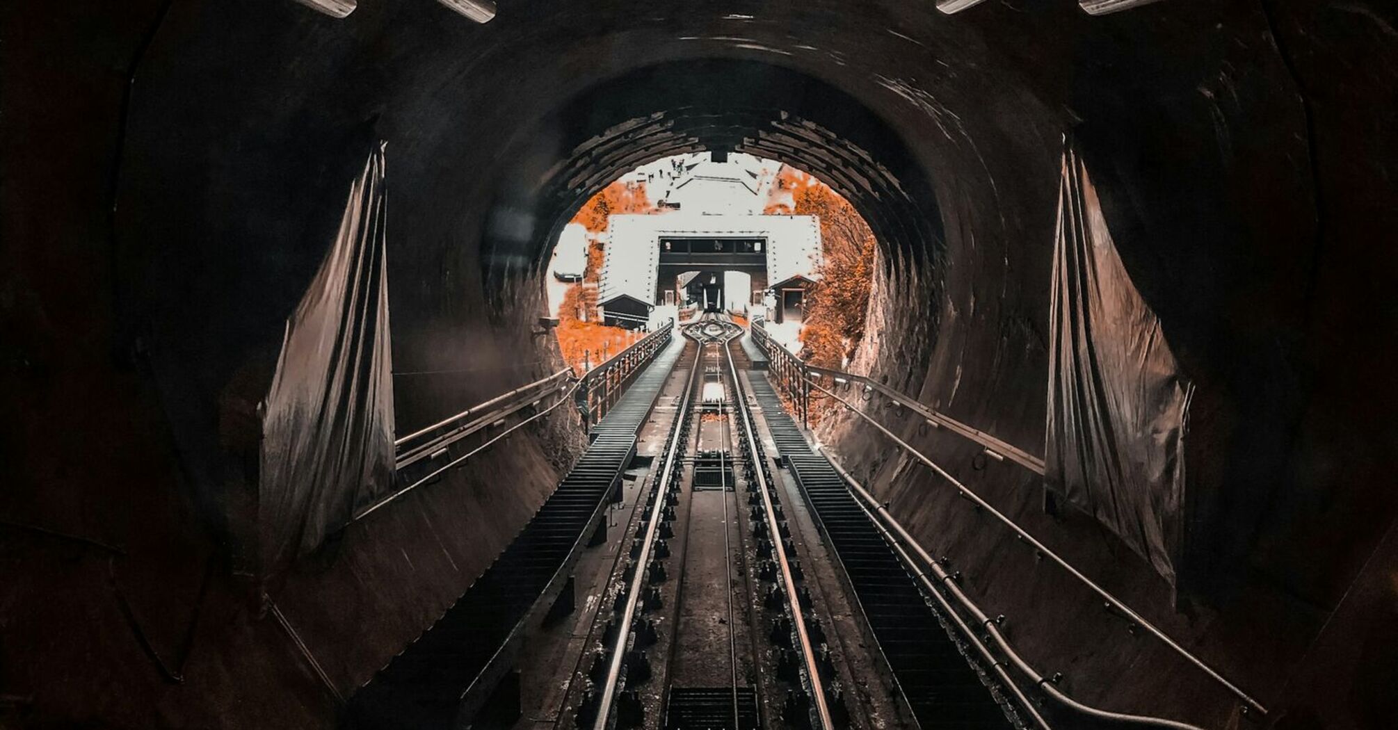 View inside a dark railway tunnel with tracks leading towards the exit