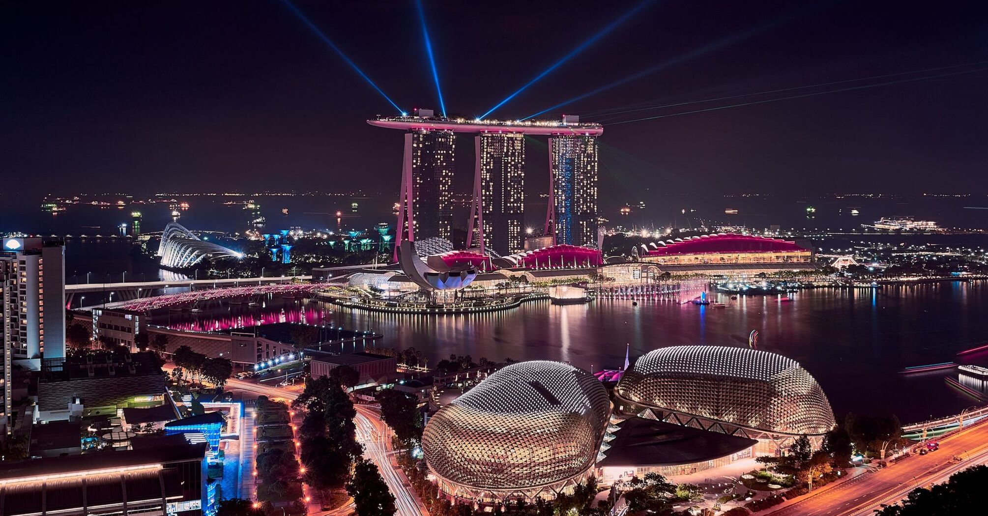 A nighttime view of Marina Bay Sands in Singapore, with illuminated buildings and laser lights over the bay