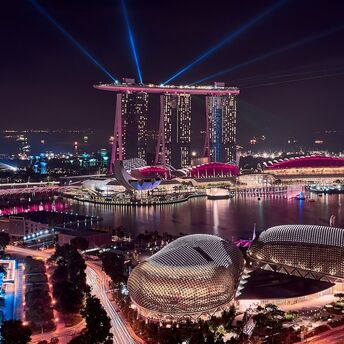 A nighttime view of Marina Bay Sands in Singapore, with illuminated buildings and laser lights over the bay