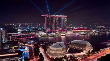 A nighttime view of Marina Bay Sands in Singapore, with illuminated buildings and laser lights over the bay