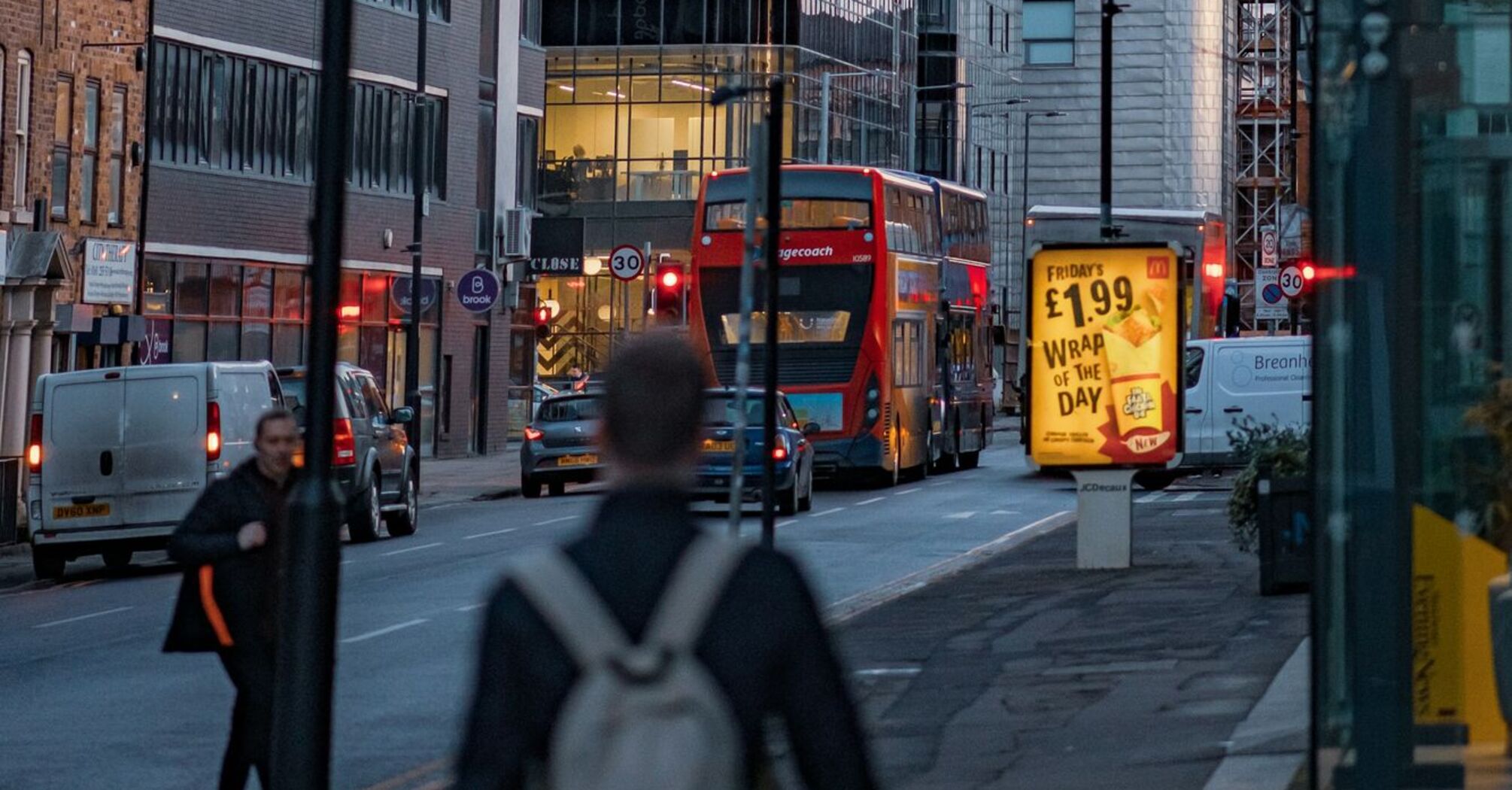 A busy street in Manchester with modern buildings and double-decker buses at dusk