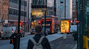 A busy street in Manchester with modern buildings and double-decker buses at dusk