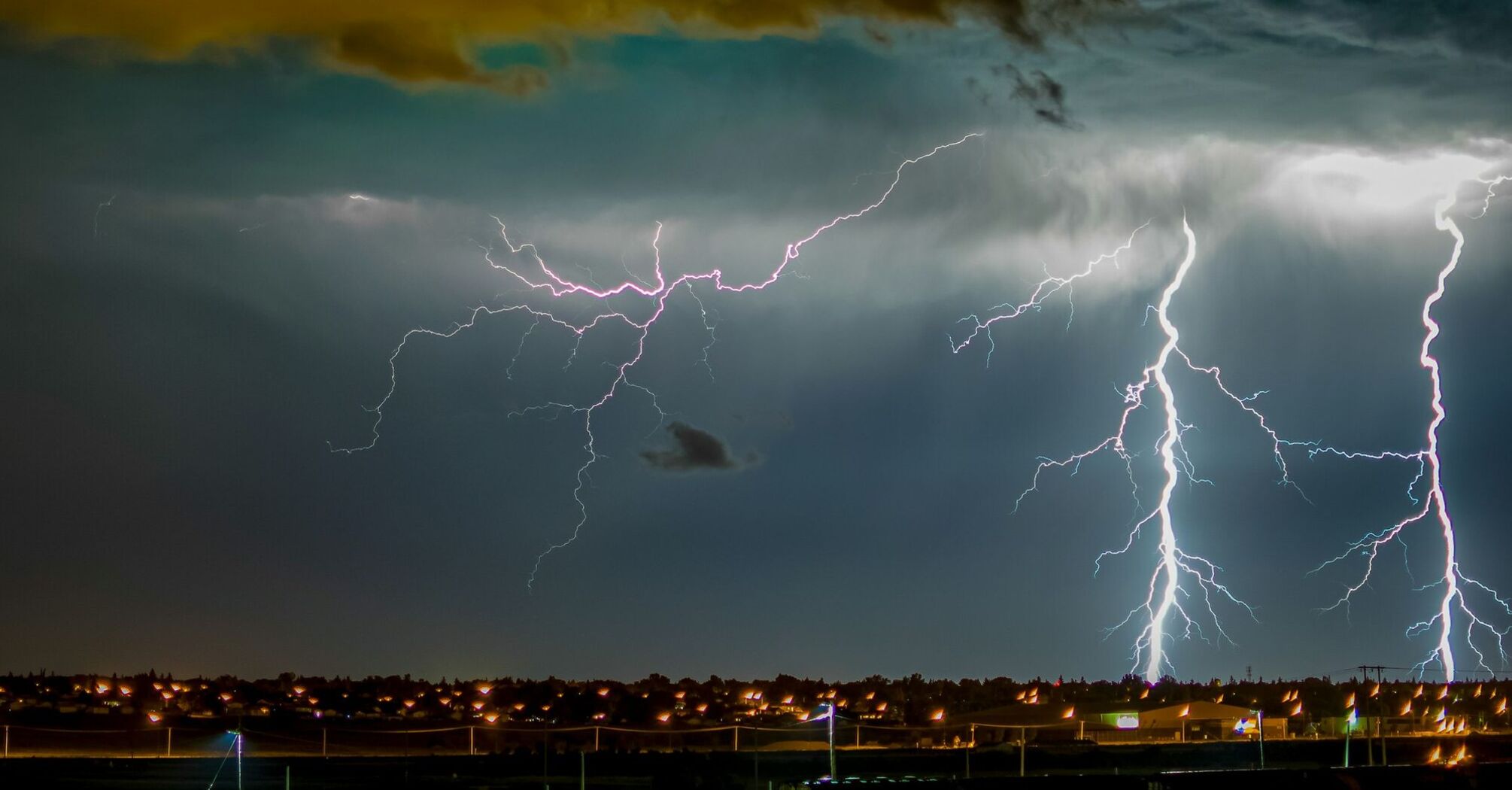 Dramatic lightning strikes illuminate a dark sky over a cityscape during a storm