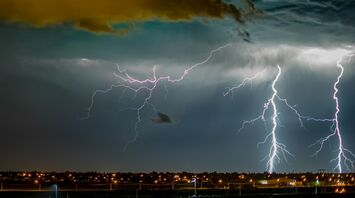 Dramatic lightning strikes illuminate a dark sky over a cityscape during a storm