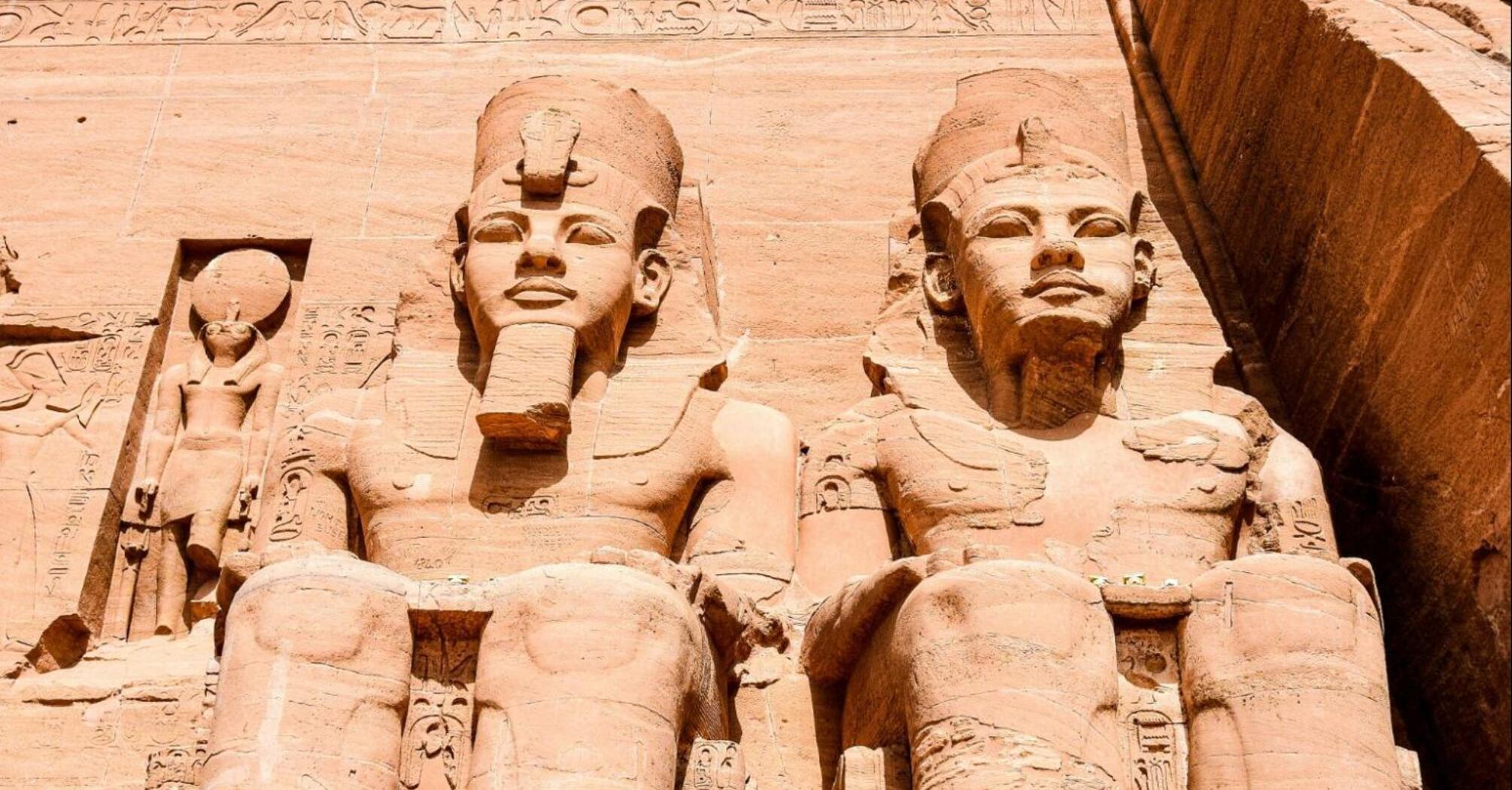 Statues of pharaohs and deities carved into the facade of the Great Temple at Abu Simbel, showcasing ancient Egyptian craftsmanship under a clear blue sky