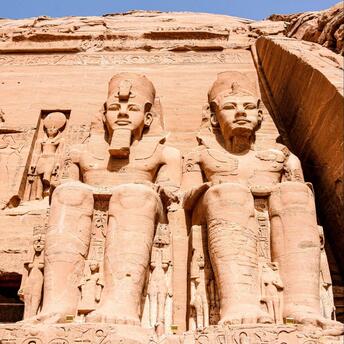 Statues of pharaohs and deities carved into the facade of the Great Temple at Abu Simbel, showcasing ancient Egyptian craftsmanship under a clear blue sky