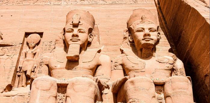 Statues of pharaohs and deities carved into the facade of the Great Temple at Abu Simbel, showcasing ancient Egyptian craftsmanship under a clear blue sky