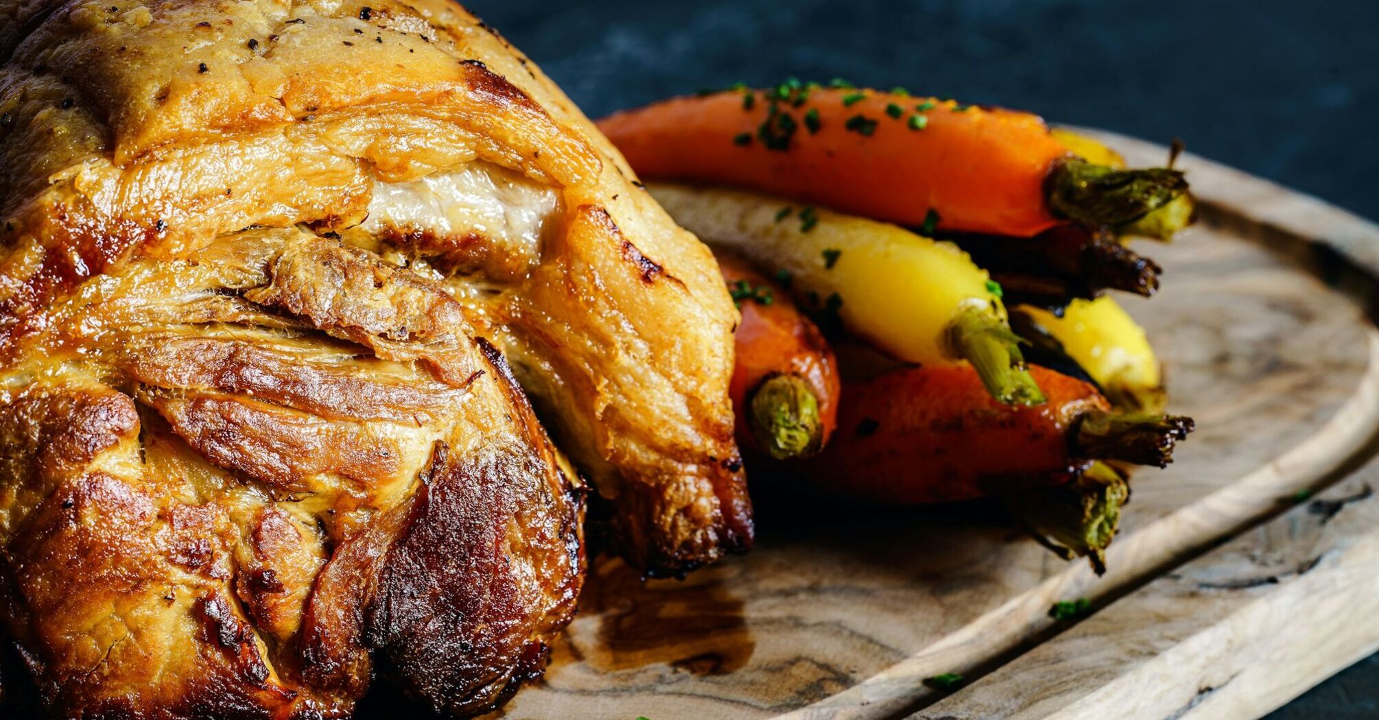 Roast meat with colorful carrots served on a wooden board