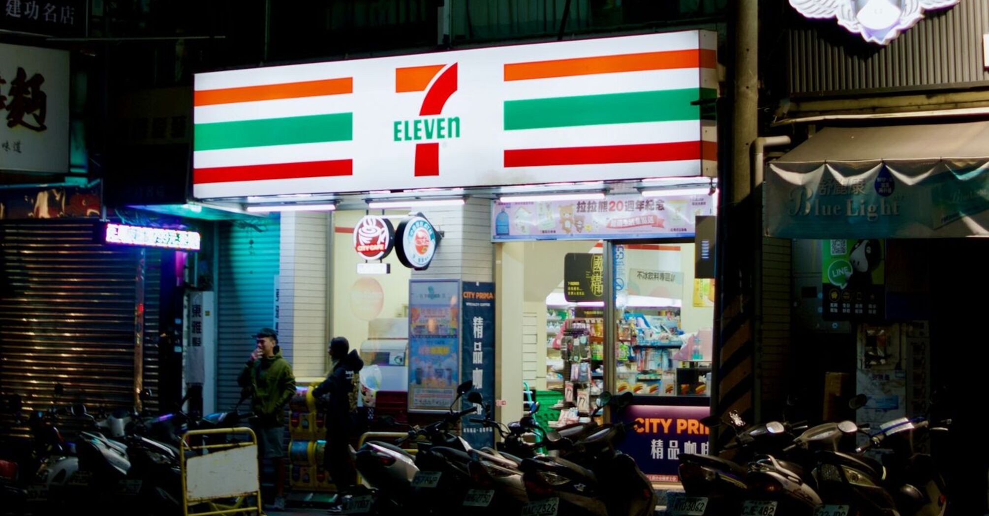 Night view of a 7-Eleven convenience store with motorcycles parked outside