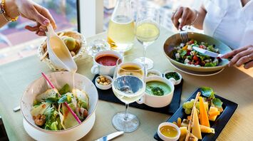 A table set with salads, sauces, cheese, and wine, showcasing a culinary dining experience