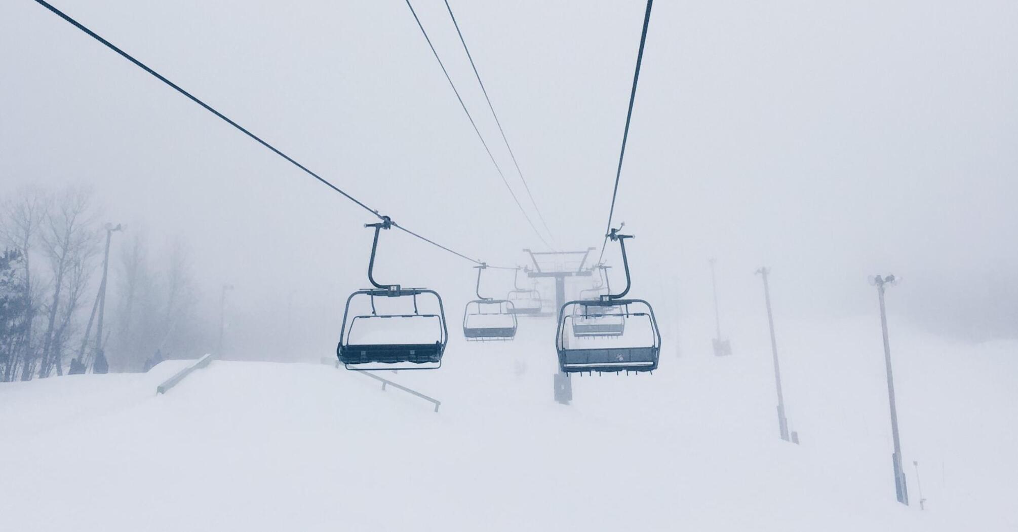 Ski lifts ascending through heavy fog on a snow-covered mountain