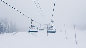 Ski lifts ascending through heavy fog on a snow-covered mountain