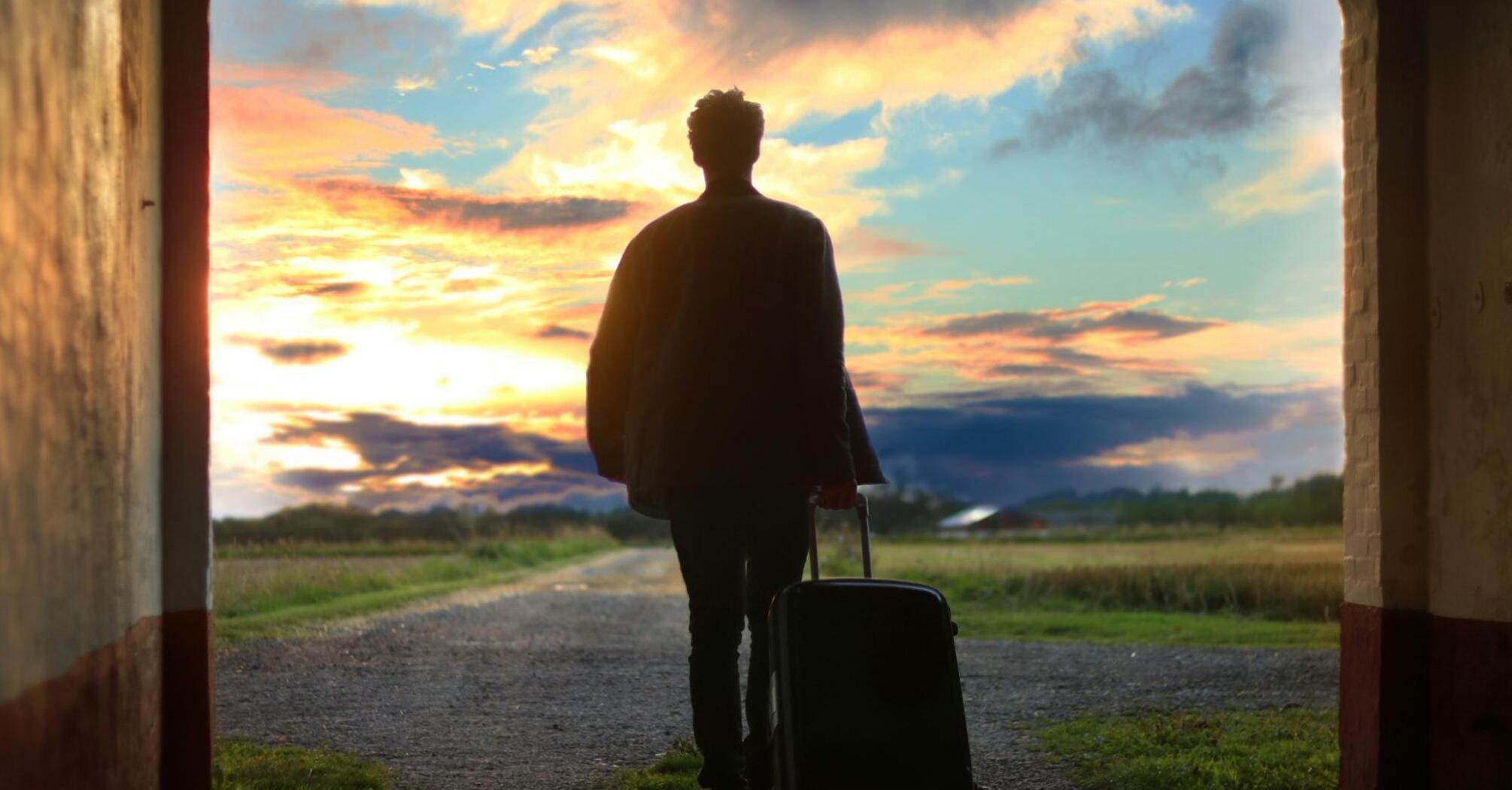 A silhouette of a traveler with a suitcase walking toward a sunset horizon through an archway, symbolizing the start of a journey