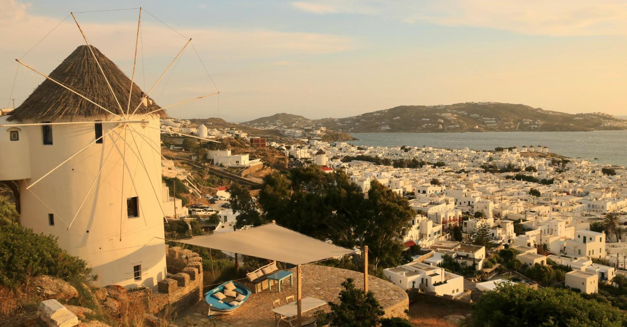 Sunset view of a traditional Mykonos windmill overlooking the white buildings of the town and the sea