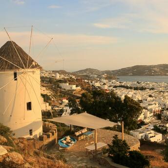 Sunset view of a traditional Mykonos windmill overlooking the white buildings of the town and the sea