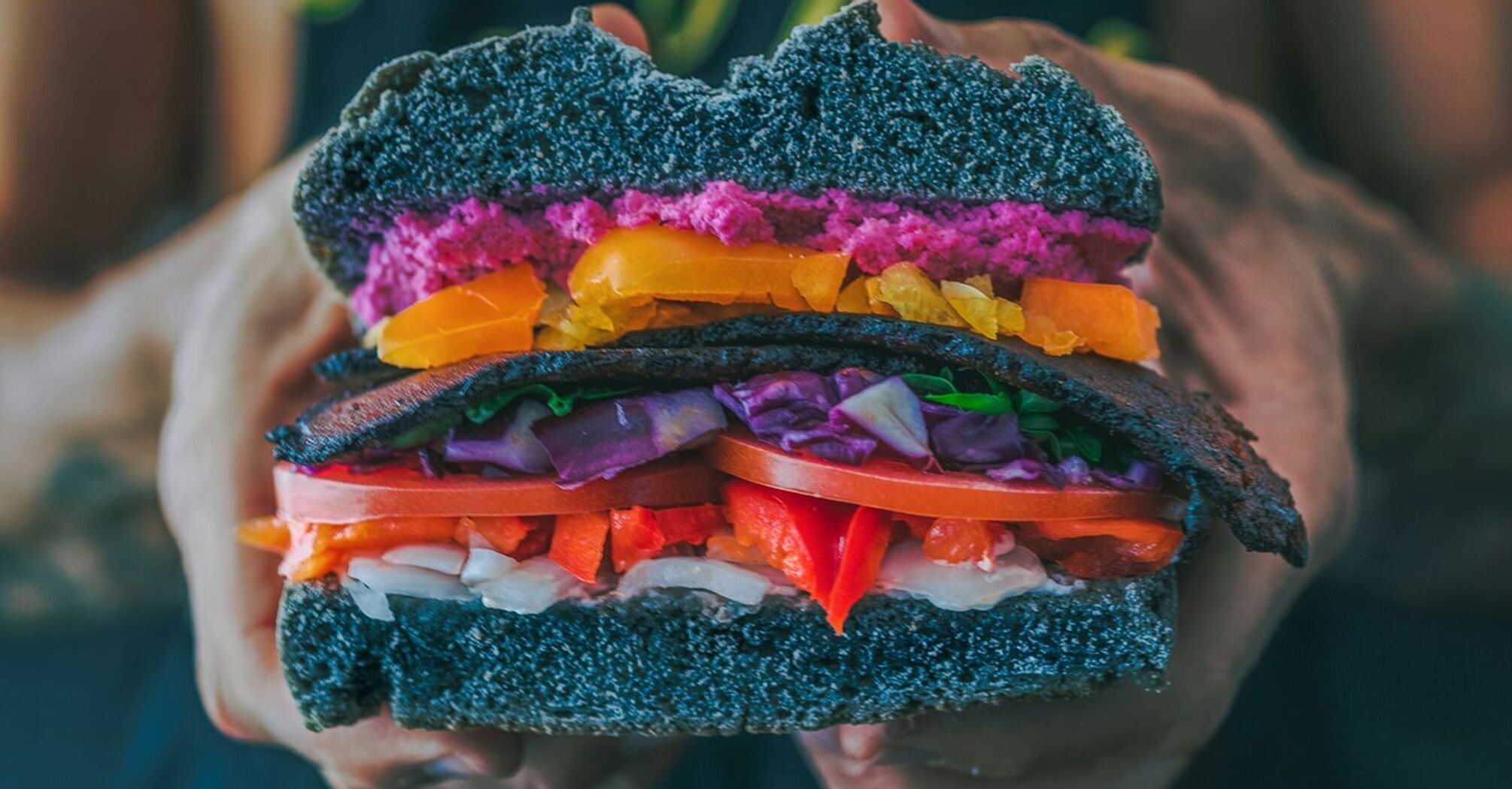 Colorful plant-based burger held by person wearing a vegan t-shirt