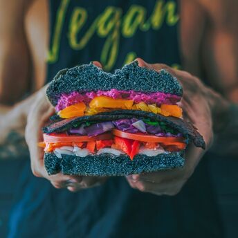 Colorful plant-based burger held by person wearing a vegan t-shirt