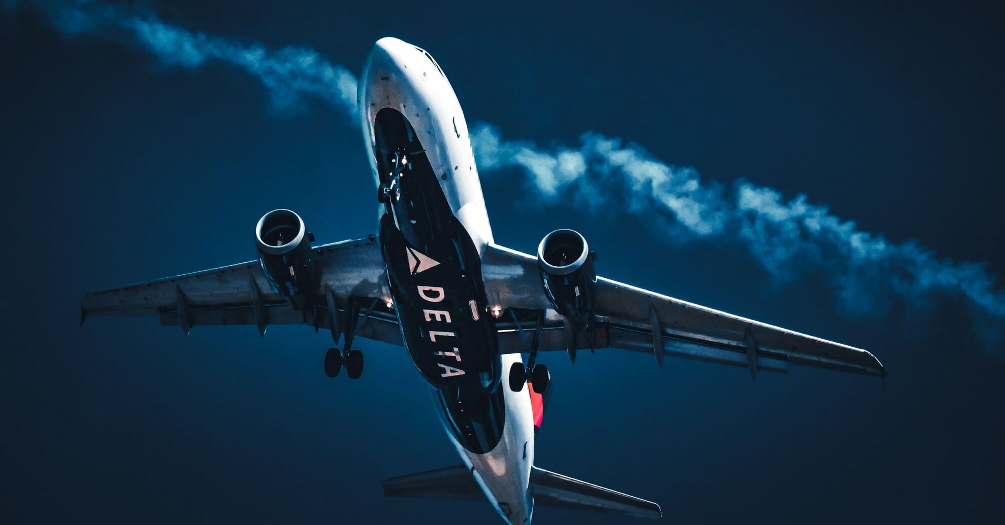 Delta airplane ascending with visible engine exhaust against a dark blue sky