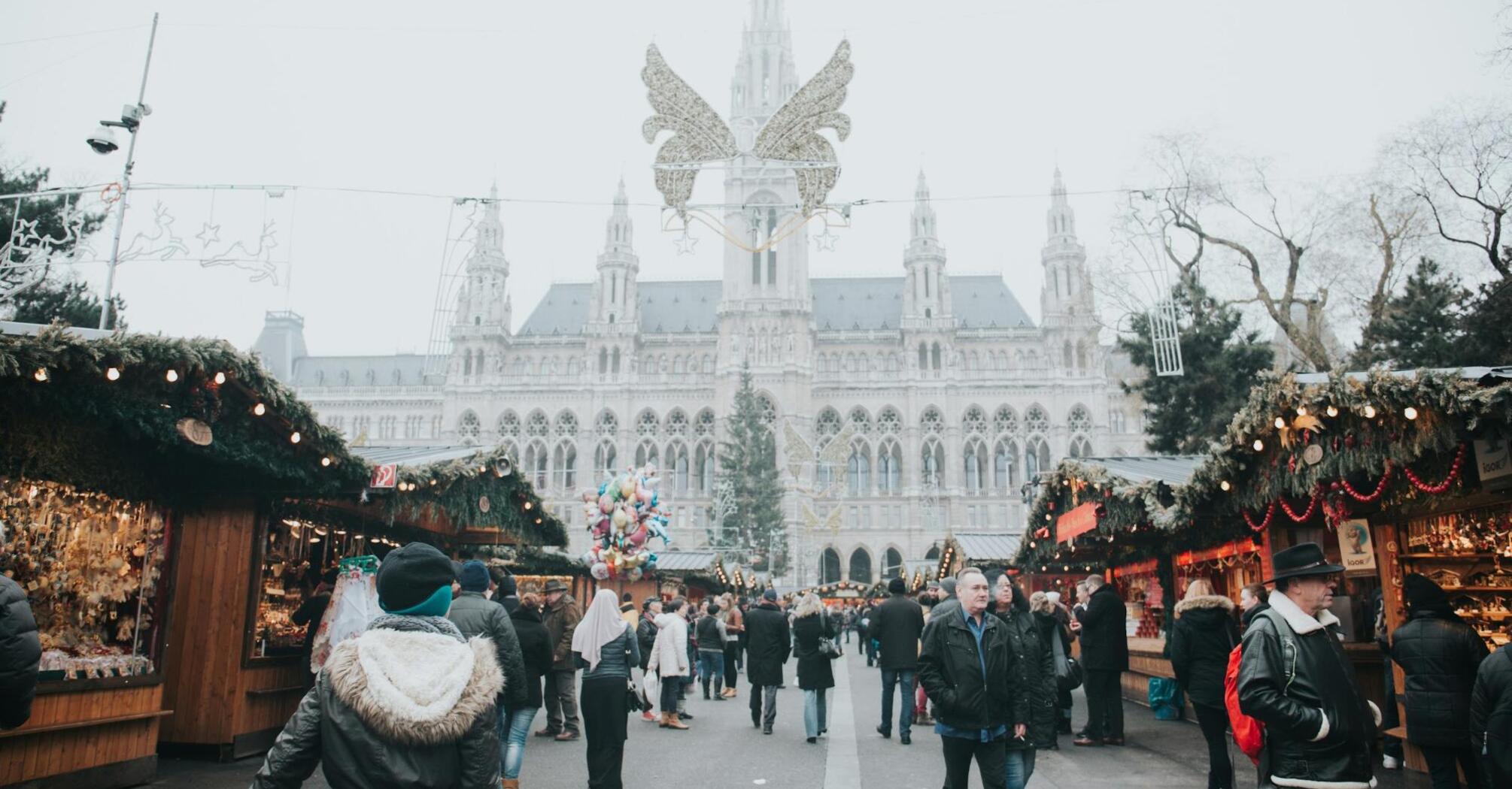 A bustling Christmas market in Vienna, with people exploring festive stalls and the grand city hall in the background