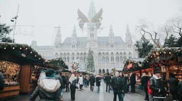 A bustling Christmas market in Vienna, with people exploring festive stalls and the grand city hall in the background