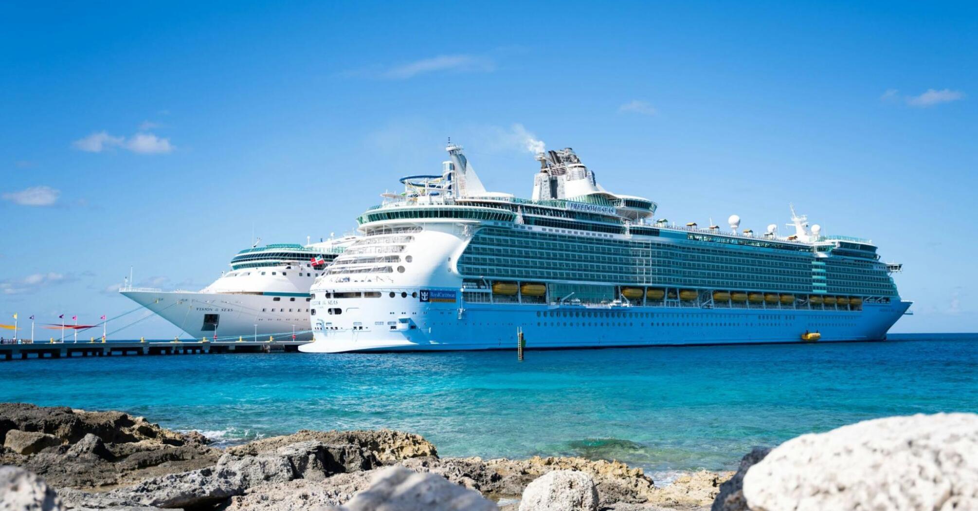 Two Royal Caribbean cruise ships docked at a scenic port with clear blue water and bright skies