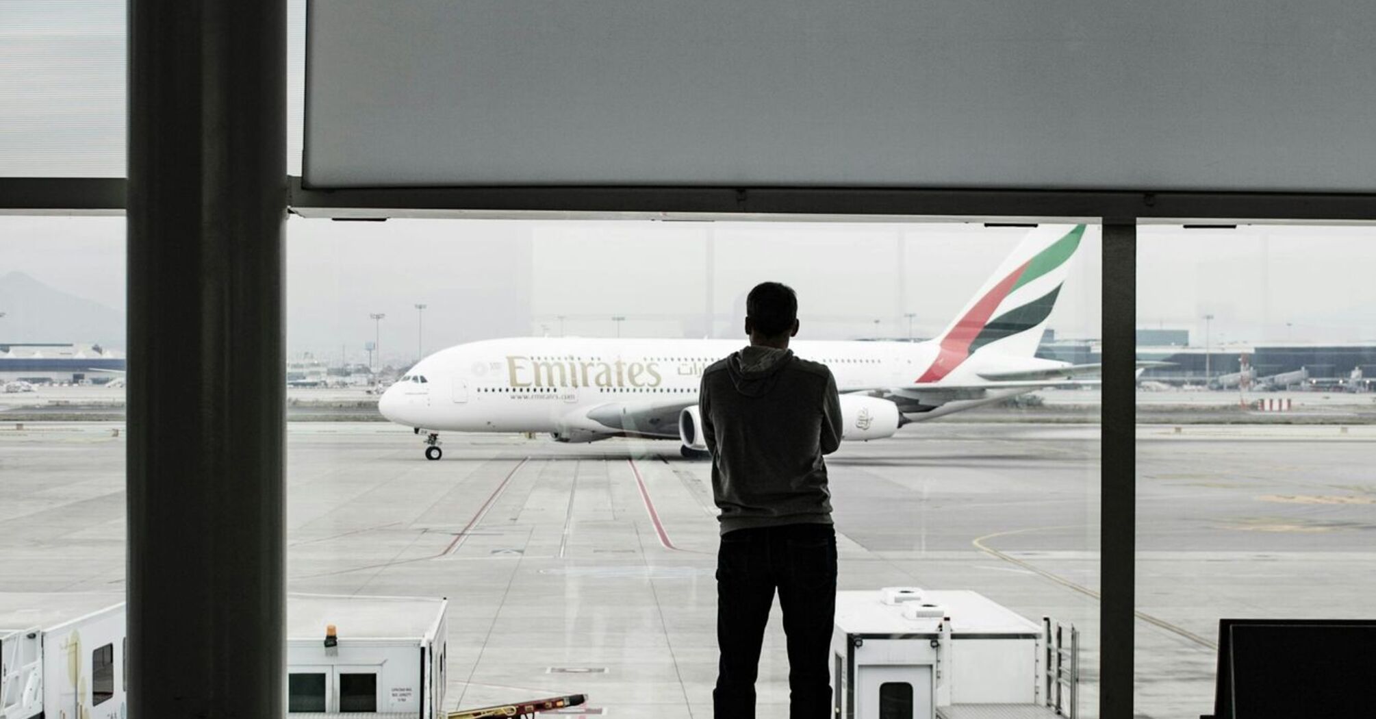 A traveler observes an Emirates aircraft from an airport terminal window