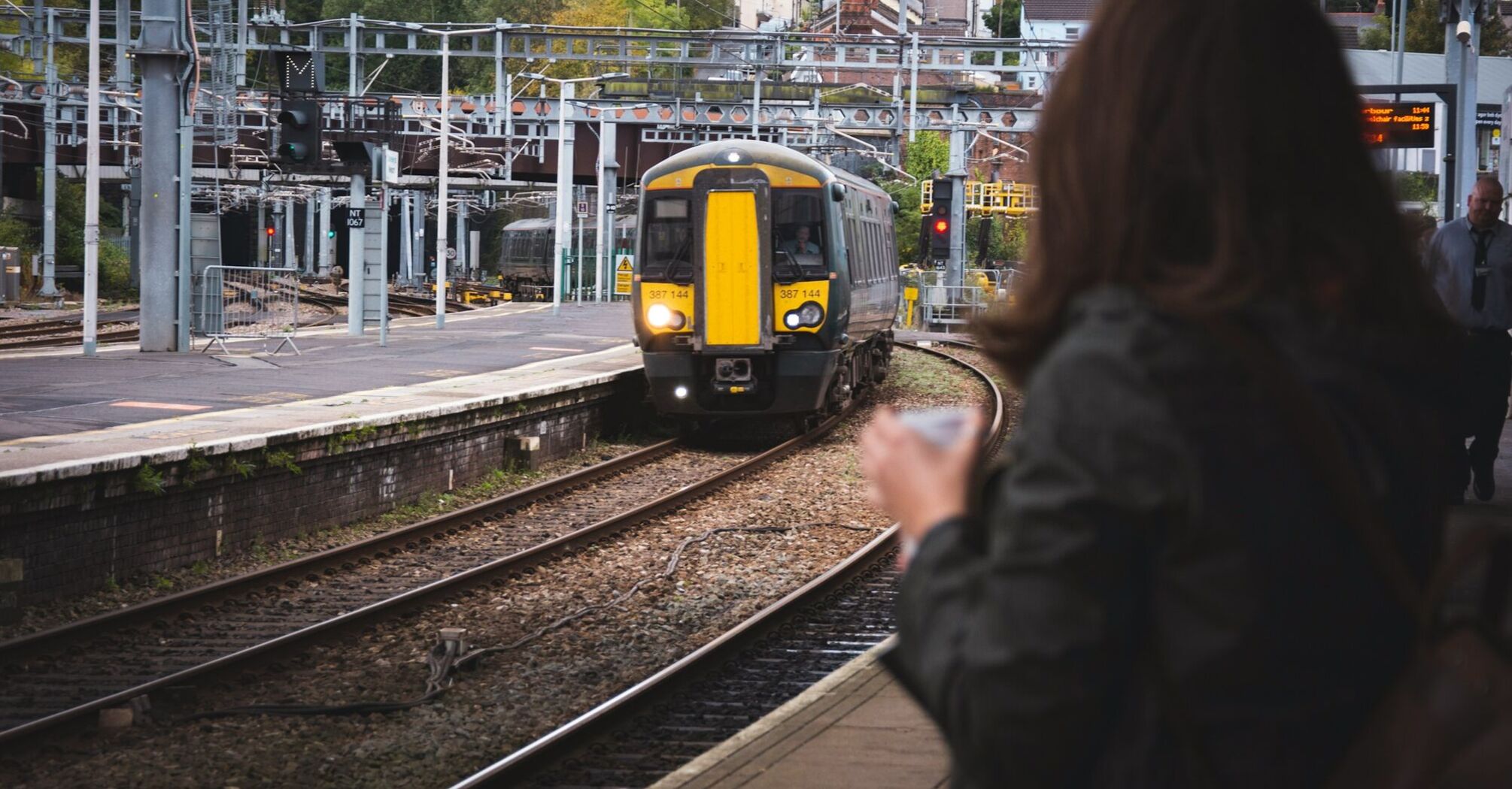 A train approaching a station as a passenger waits on the platform