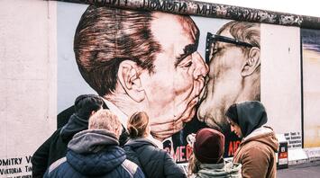 Tourists observing a mural at Berlin’s East Side Gallery, depicting a famous historical image on a remnant of the Berlin Wall