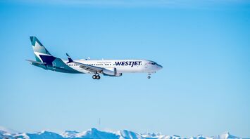 A WestJet airplane in flight with snow-capped mountains in the background