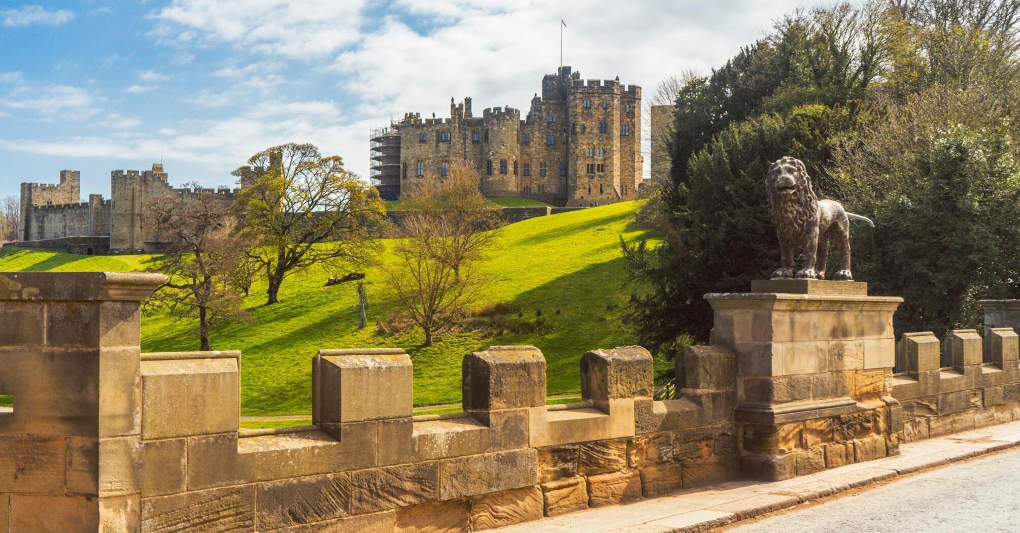 Alnwick Castle on a sunny day with a lion statue in foreground