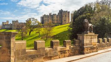 Alnwick Castle on a sunny day with a lion statue in foreground