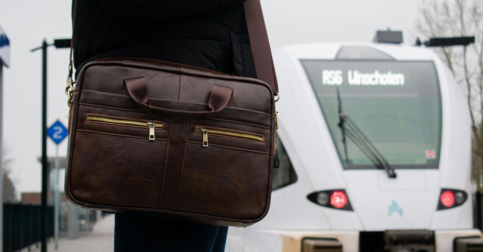 Person with leather bag waiting at a train station with a train approaching in the background