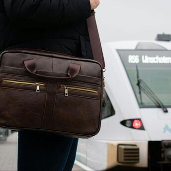 Person with leather bag waiting at a train station with a train approaching in the background