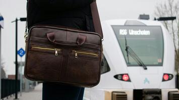 Person with leather bag waiting at a train station with a train approaching in the background