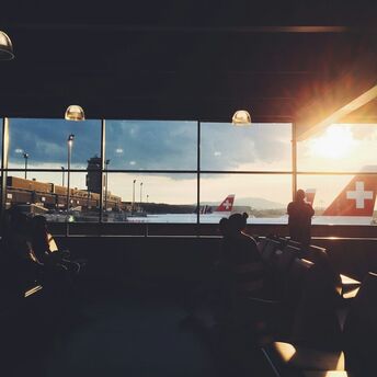 Passengers at an airport terminal with SWISS planes visible through large windows during sunset