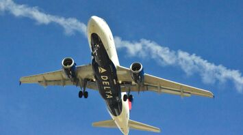 A Delta airplane ascending into a clear blue sky