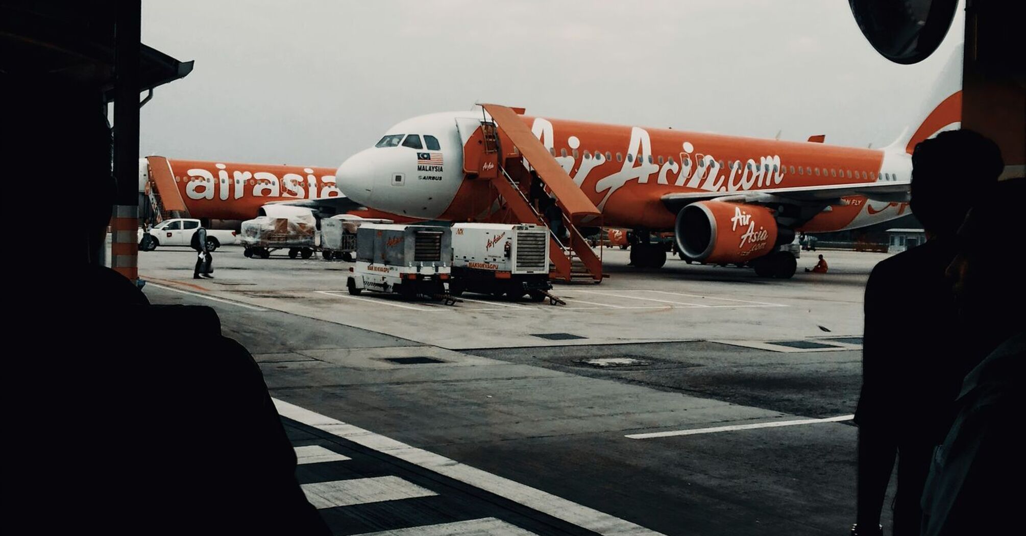 AirAsia aircraft parked at an airport gate during dusk, with ground crew preparing the plane for operations