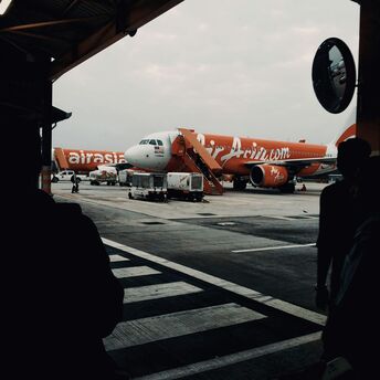 AirAsia aircraft parked at an airport gate during dusk, with ground crew preparing the plane for operations