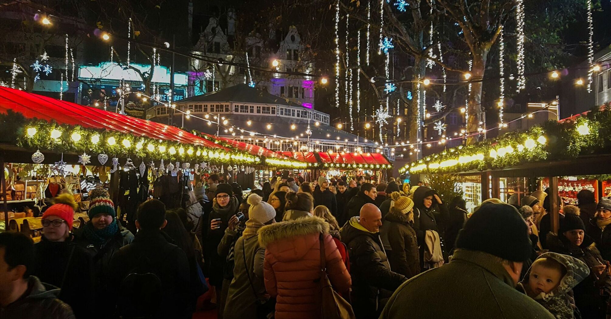 Festive crowd enjoying a Christmas market with decorated stalls and lights