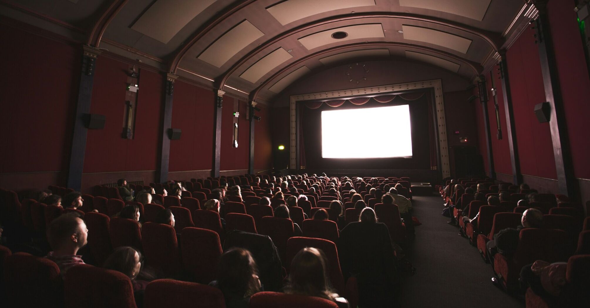 Audience seated in a classic cinema hall watching a movie on a large screen