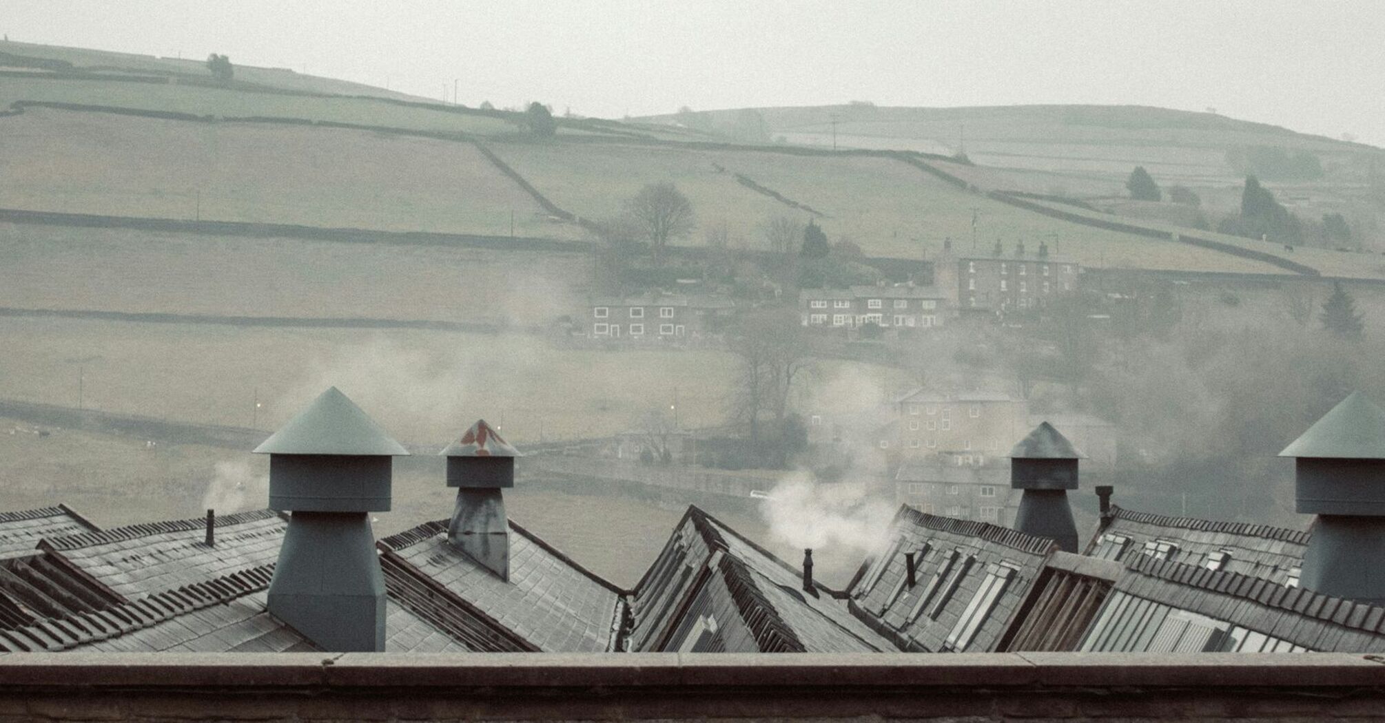 A foggy, wintry landscape with rooftops and distant hills