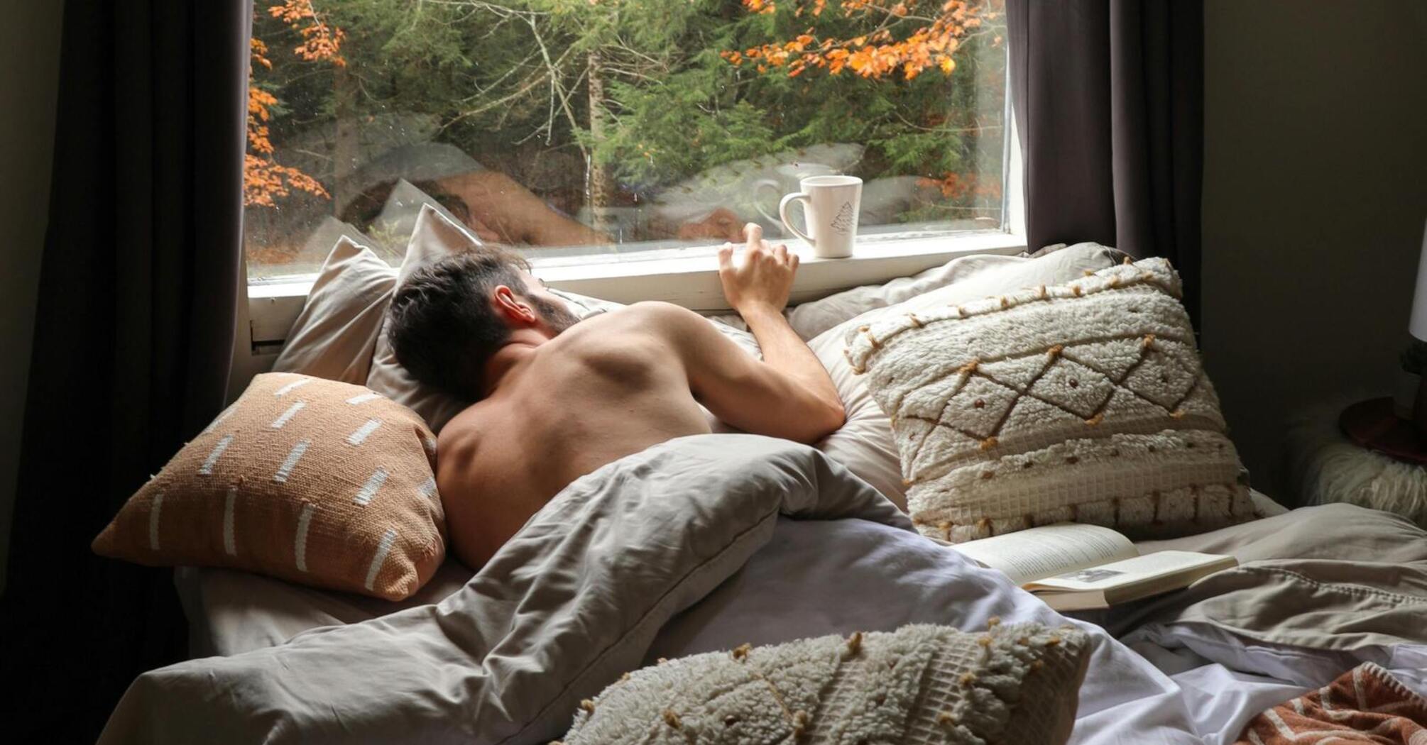 Man resting in bed with a view of autumn forest through a large window