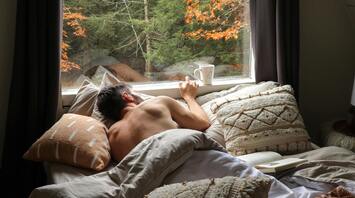 Man resting in bed with a view of autumn forest through a large window