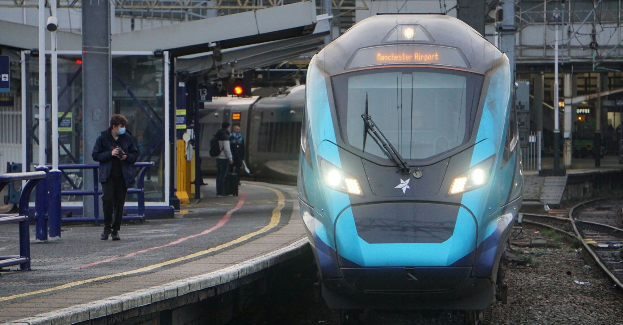 A TransPennine Express train at a station platform with passengers nearby