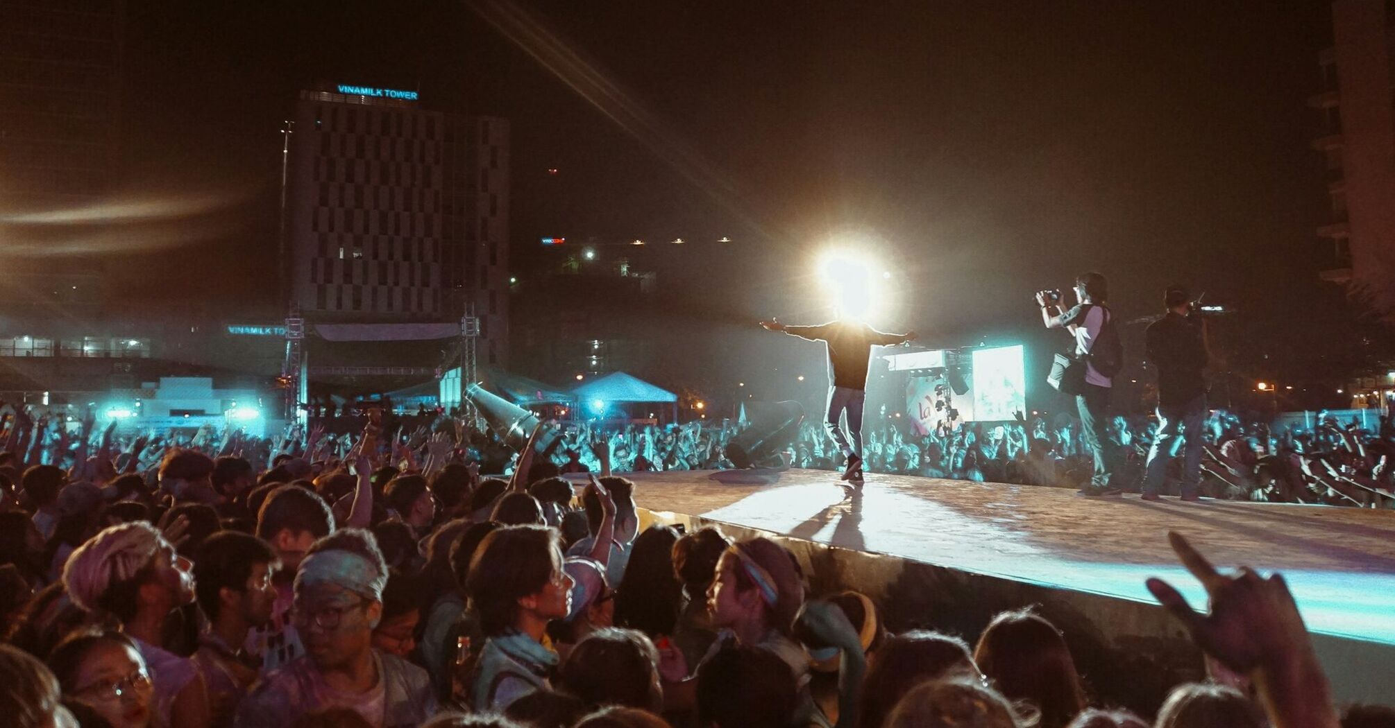 A large crowd at a night concert with bright lights and a performer on stage